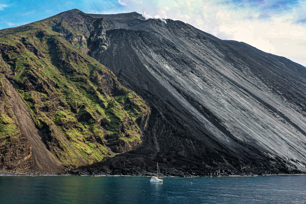 The&nbsp;Victoria, the Gombessa team’s trimaran, anchored in front of Stromboli. Behind, you can clearly see the boundary between the Sciara (or ‘road of fire’ in Arabic) and the green slopes covered with vegetation that the lava flows have spared.
