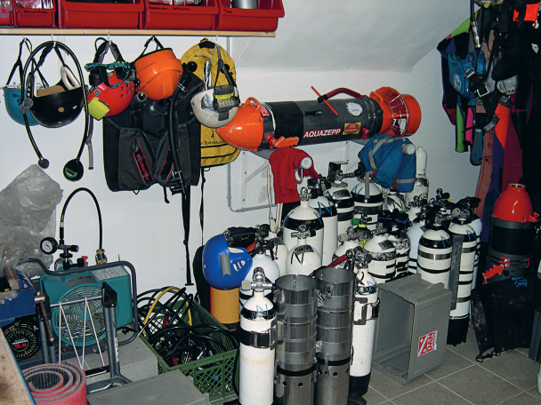 A tech diver’s garage, featuring numerous tanks for different gases, a scooter, a compressor, etc.
